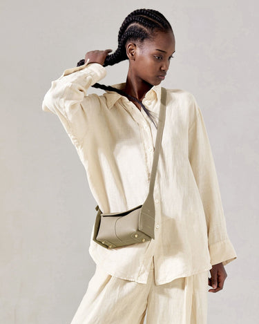 Pebbled leather Mini Drippy Roof Bag in Cobble, crossbody style with gold hardware, worn with a linen outfit.