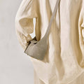 Mini Drippy Roof Bag in Cobble color, a pebbled leather crossbody bag with architectural design, worn with a linen outfit.