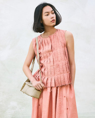 Mini Drippy Roof Bag in Ivory, textured leather crossbody bag with flap, worn with pleated pink outfit.