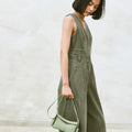 Pale green mini drippy roof bag, full-grain leather, with adjustable strap, held by woman in olive green jumpsuit.