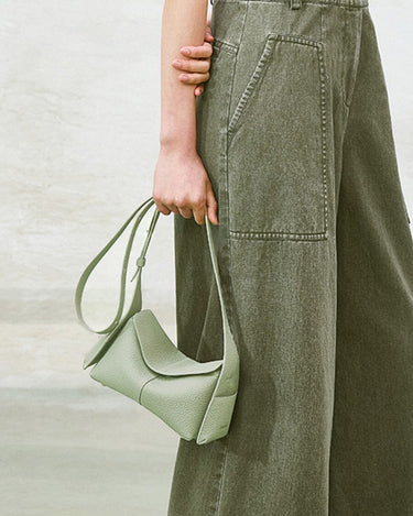Light green full-grain leather mini drippy roof bag with adjustable strap worn by a person in olive green pants.