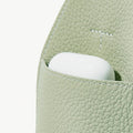 Sage green full-grain leather mini drippy roof bag with white earbuds peeking out.