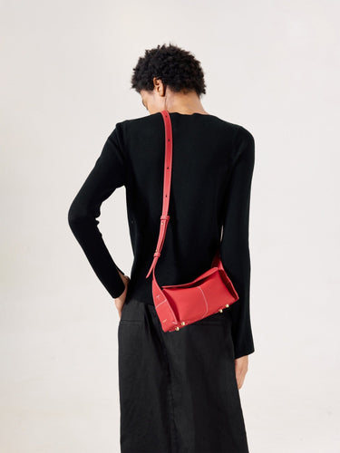 Red full-grain leather mini drippy roof bag with white stitching and gold hardware, worn by a woman.