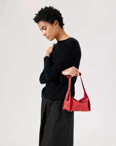 Red full-grain leather Mini Drippy Roof Bag with white stitching and a unique angular design, held by a woman.
