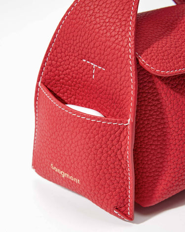 Red full-grain leather mini bag with white stitching and gold 'Songmont' logo. Features exterior pocket.