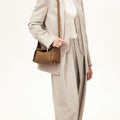 Mini Drippy Roof Bag in Mocha, made of full-grain leather with gold hardware, worn by a model in a beige suit.