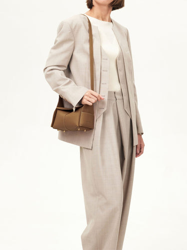 Mini Drippy Roof Bag in Mocha, made of full-grain leather with gold hardware, worn by a model in a beige suit.