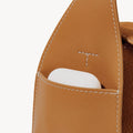 Mini Drippy Roof Bag in Sea Buckthorn nubuck leather with a white earbud case in the front pocket. Features debossed Songmont logo.