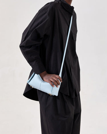 Light blue full-grain leather Mini Drippy Roof Bag with gold hardware, worn crossbody.