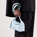 Light blue leather mini bag with folded flap, "Songmont" branding, held by person in black.