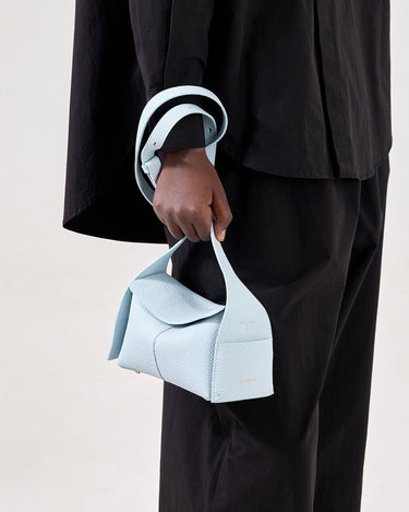 Light blue leather mini bag with folded flap, "Songmont" branding, held by person in black.