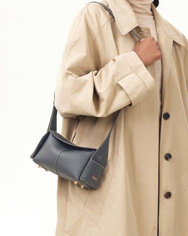 Mini Drippy Roof Bag in dark grey pebbled leather with white stitching and gold hardware, worn with a trench coat.