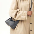 Woman in a beige trench coat carrying a navy blue Mini Drippy Roof Bag with gold hardware.