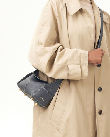 Woman in a beige trench coat carrying a navy blue Mini Drippy Roof Bag with gold hardware.