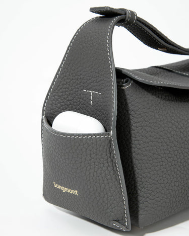 Mini Drippy Roof Bag in Stardust grey pebbled leather with white stitching and an exterior pocket holding white earbuds.