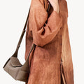 Taupe Mini Drippy Roof Bag on a woman wearing a textured brown shirt. Pebbled leather handbag with flap closure.