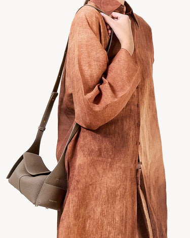Taupe Mini Drippy Roof Bag on a woman wearing a textured brown shirt. Pebbled leather handbag with flap closure.