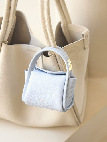 Sky Mini Song AirPods Case in textured leather with gold hardware, attached to a beige tote bag.