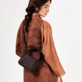 Mini Song Bag in Burgundy: A structured, pebbled leather handbag with gold hardware, worn by a woman.