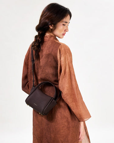Mini Song Bag in Burgundy: A structured, pebbled leather handbag with gold hardware, worn by a woman.