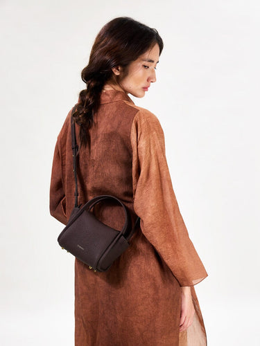 Mini Song Bag in Burgundy: A structured, pebbled leather handbag with gold hardware, worn by a woman.