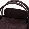 Close-up of the burgundy Mini Song Bag showing its pebbled leather texture, double handles, and interior flap.