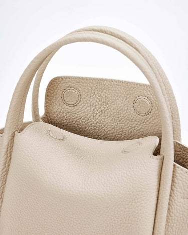 Close-up of the ivory Mini Song Bag, showcasing its textured full-grain leather, rounded handles, and structured opening.