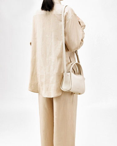 Ivory mini song bag made of textured full-grain leather, worn by a woman in a beige linen outfit.