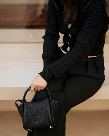 Black Mini Song Bag in textured leather with gold hardware, held by a person in black attire.