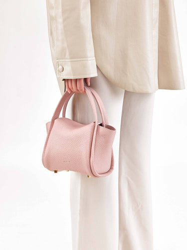 Pink full-grain leather Mini Song Bag with gold hardware, held by a hand.