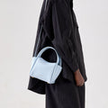 Sky blue pebbled leather Mini Song Bag with gold hardware, carried by a model in a black oversized shirt.
