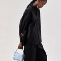 Mini Song Bag in Sky blue pebbled leather, held by a woman in a black outfit.