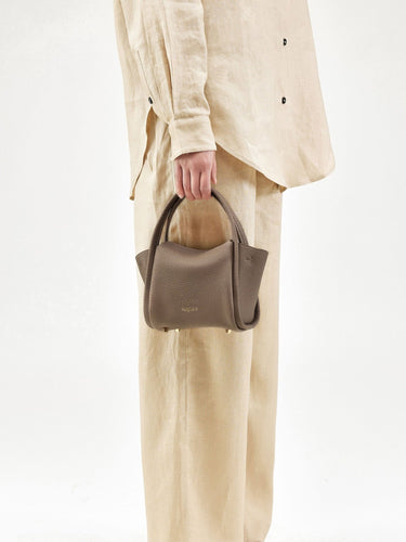 Taupe pebble-grained leather Mini Song Bag held by a person in beige linen attire