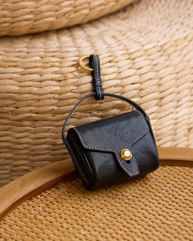 Mini Yore black leather AirPods case with white stitching and gold clasp.