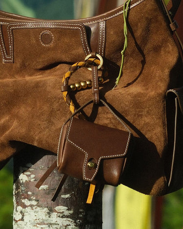 Mini Yore AirPods Case in Sandal color, made of vegetable-tanned leather, attached to a brown suede bag with leather trim.