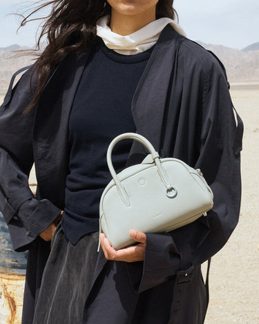 Celeste Mini Yore Bowling Bag crafted from pebbled full-grain leather with silver hardware, held by a woman in a desert.