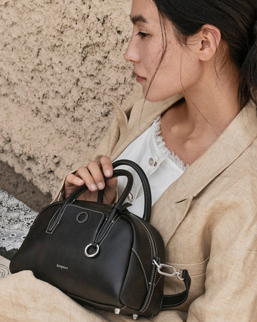 Woman holding black Mini Yore Bowling Bag by Songmont, made of full-grain leather with white stitching.