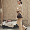 Mini Yore Bowling Bag in dark brown leather with silver hardware and white stitching, worn by a model in a beige suit.