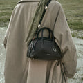 Ebony Mini Yore Bowling Bag in full-grain leather, white stitching, silver hardware, worn with taupe trench coat.