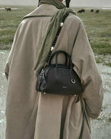 Ebony Mini Yore Bowling Bag in full-grain leather, white stitching, silver hardware, worn with taupe trench coat.