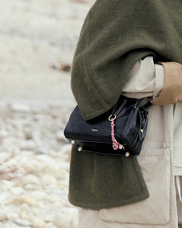 Mini Yore Duffle Bag in Onyx, black leather crossbody bag with white stitching and braided charm.