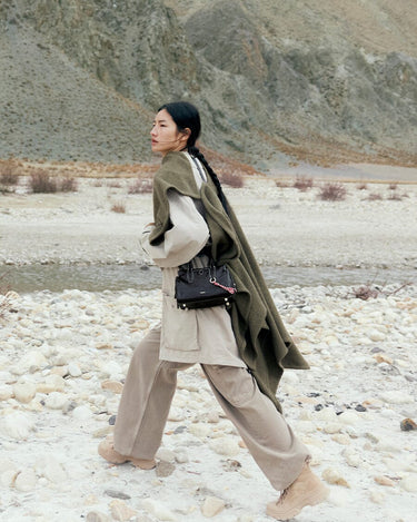 Mini Yore Duffle Bag in Onyx black leather, worn by a woman in a rocky outdoor setting.