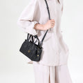 Black Mini Yore Duffle Bag made of vegetable-tanned leather with contrast stitching, worn crossbody by a woman in linen.