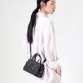 Mini Yore Duffle Bag in Onyx: black vegetable-tanned leather with white stitching and gold hardware, worn on shoulder.