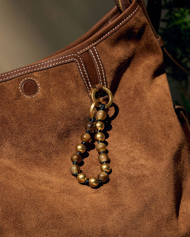 Topaz peace beads charm with golden and brown beads on a brown suede bag.