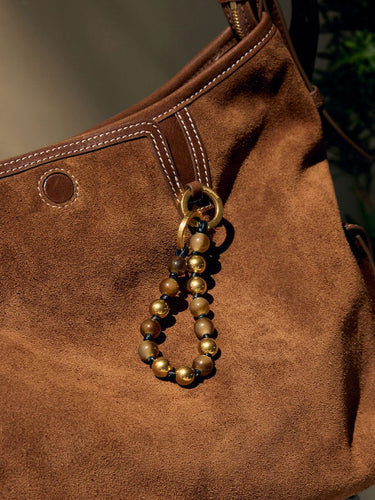 Topaz peace beads charm with golden and brown beads on a brown suede bag.