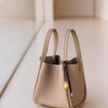 Beige leather tote bag with a dark brown leather strap and gold hardware detail.