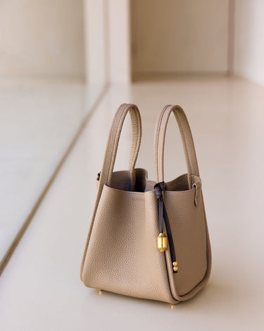 Beige leather tote bag with a dark brown leather strap and gold hardware detail.