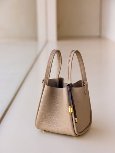 Beige leather tote bag with a dark brown leather strap and gold hardware detail.