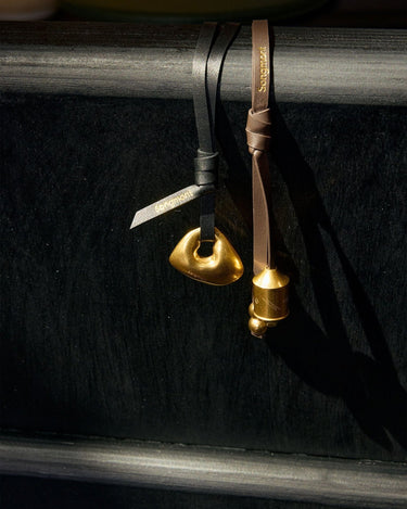 Gold abstract charm on black leather and gold prayer wheel charm on brown leather.